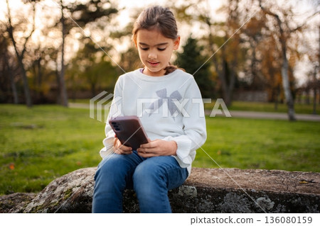Girl sitting in park using mobile phone Girl sitting in park using mobile phone 136080159