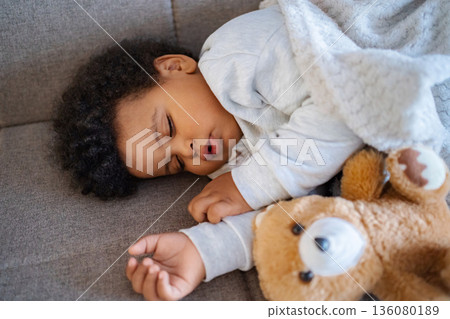 Baby sleeping peacefully with teddy bear on couch 136080189