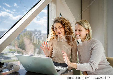 Happy women waving during online video call on laptop Happy women waving during online video call on laptop 136080197