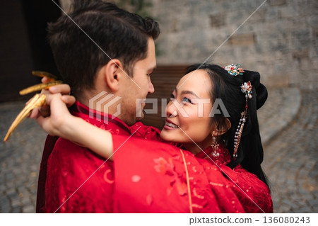 Interracial couple embracing during traditional Chinese wedding ceremony 136080243