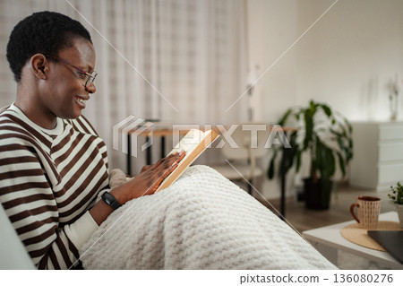 Happy black woman enjoying cozy time reading book at home 136080276