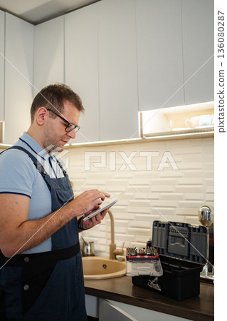 Handyman using tablet near toolbox in modern kitchen Handyman using tablet near toolbox in modern kitchen 136080287