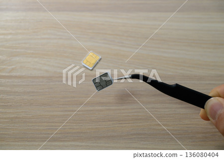 Hand holding a SIM card with tweezers Hand holding a SIM card with tweezers 136080404