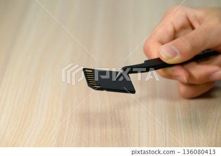 Hand holding up an SD card with tweezers 136080413