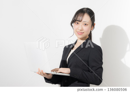 A young woman in a suit holding a laptop. Business image of new graduates and job hunting. Job hunting recruitment image. Looking at the camera. A young woman in a suit holding a laptop. Business image of new graduates and job hunting. Job hunting recruitment image. Looking at the camera. 136080506
