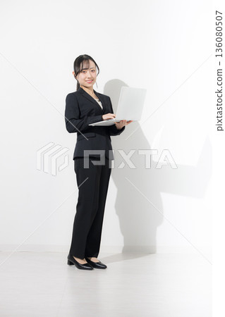 Young woman in a suit holding a laptop. Business image of new graduates and new employment. Job hunting recruitment image. Looking at the camera. White background. Young woman in a suit holding a laptop. Business image of new graduates and new employment. Job hunting recruitment image. Looking at the camera. White background. 136080507