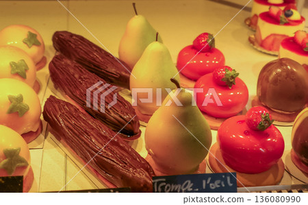 Parisian bakery window showcasing various gourmet desserts, including pear shaped pastries and shiny red strawberry cakes 136080990