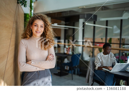 Confident businesswoman smiling in modern office coworking space 136081188