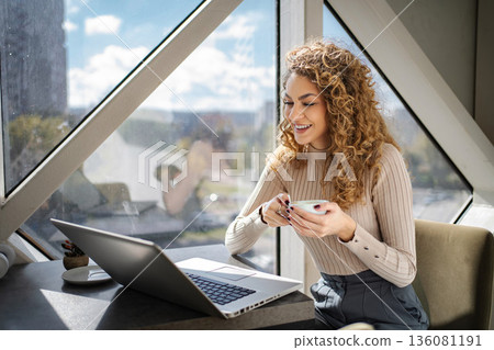 Young woman smiling working on laptop with coffee Young woman smiling working on laptop with coffee 136081191
