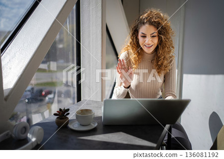 Woman waving during video call using laptop in cafe 136081192