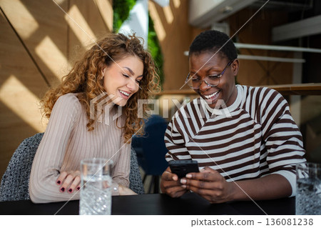 Women friends laughing using smartphone in cafe 136081238