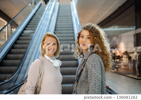Two women friends smiling on escalator in shopping mall Two women friends smiling on escalator in shopping mall 136081262