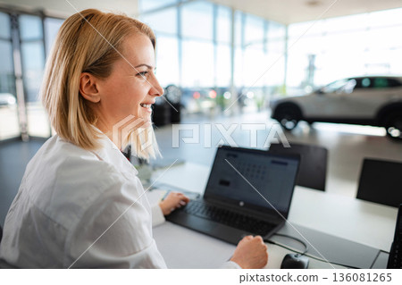 Smiling saleswoman working in car dealership showing new vehicles Smiling saleswoman working in car dealership showing new vehicles 136081265