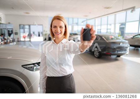 Saleswoman holding car key celebrating new vehicle purchase 136081268