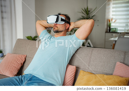 Man enjoying virtual reality experience on living room couch Man enjoying virtual reality experience on living room couch 136081419