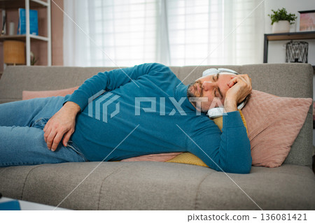 Man sleeping on couch wearing headphones relaxing at home 136081421