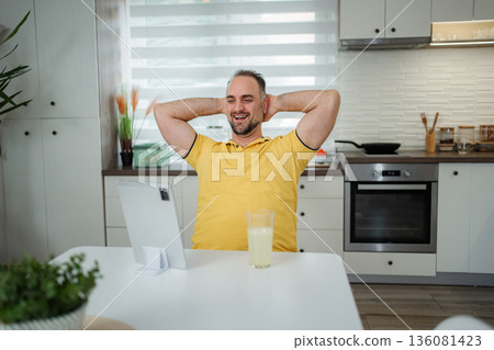 Happy man relaxing in kitchen enjoying digital tablet Happy man relaxing in kitchen enjoying digital tablet 136081423