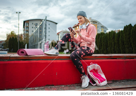 Woman checking phone after outdoor fitness workout wearing athleisure Woman checking phone after outdoor fitness workout wearing athleisure 136081429