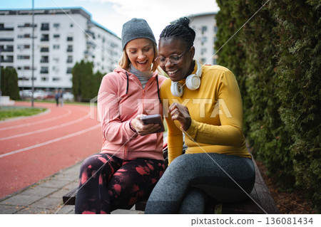 Diverse women friends looking at smartphone after workout Diverse women friends looking at smartphone after workout 136081434