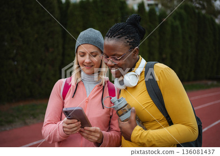 Diverse women friends looking at smartphone on track Diverse women friends looking at smartphone on track 136081437