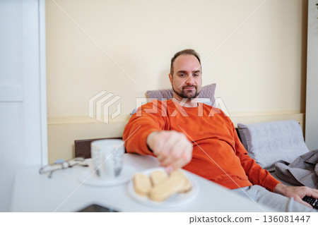 Man enjoying breakfast in bed, choosing a biscuit 136081447
