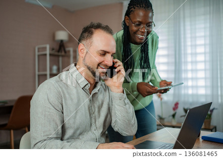 Man talking on phone while woman showing tablet at home office 136081465