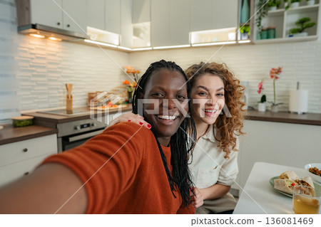 Two smiling diverse women taking selfie in home kitchen Two smiling diverse women taking selfie in home kitchen 136081469