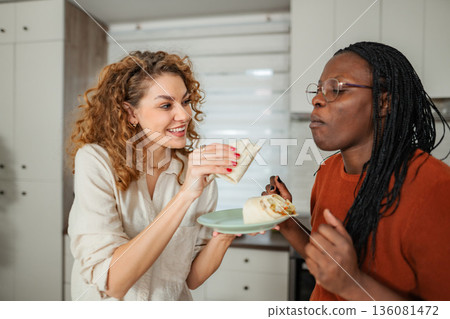 Women sharing burritos and laughing in kitchen 136081472