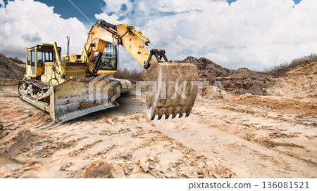 A bulldozer and excavator are pictured at a construction site working in a sand pit and earthworks, under partly cloudy skies. Dust is present as the earth is moved A bulldozer and excavator are pictured at a construction site working in a sand pit and earthworks, under partly cloudy skies. Dust is present as the earth is moved 136081521