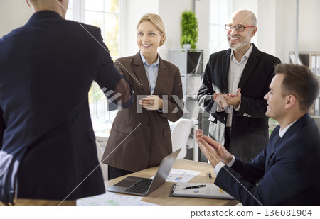 Professional handshake in modern office as coworkers clap and celebrate deal 136081904
