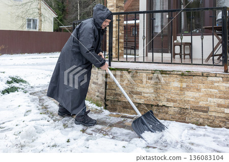 Senior male removing snow near house and garden highlighting cold weather routine and physical activity. Senior male removing snow near house and garden highlighting cold weather routine and physical activity. 136083104