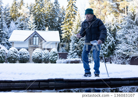 Male person near water pond throwing food to fish on snow covered landscape. Peaceful lifestyle moment on natural light scene. Male person near water pond throwing food to fish on snow covered landscape. Peaceful lifestyle moment on natural light scene. 136083107