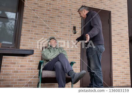 Two adult men arguing on outdoor wooden terrace near house expressing disagreement conflict and strong emotions. Two adult men arguing on outdoor wooden terrace near house expressing disagreement conflict and strong emotions. 136083159