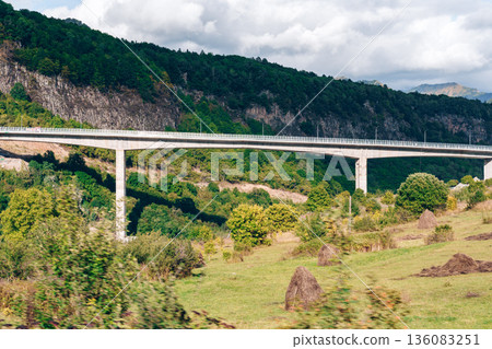 Bridge spans green valley under cloudy sky in rural landscape Bridge spans green valley under cloudy sky in rural landscape 136083251