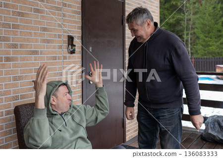 Two adult men arguing on outdoor wooden terrace near house expressing disagreement conflict and strong emotions. Two adult men arguing on outdoor wooden terrace near house expressing disagreement conflict and strong emotions. 136083333
