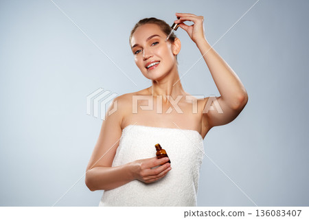 Woman applying skincare serum while holding a dropper in a simple setting 136083407