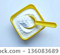 How-to cleaning blogs. Pile of powdered detergent in yellow plastic container with a measuring spoon on a white background. Home washing and cleaning. 136083689