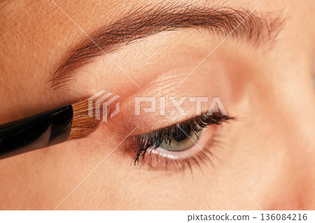 Woman applying cosmetic eyeshadow to her eye using a brush Woman applying cosmetic eyeshadow to her eye using a brush 136084216
