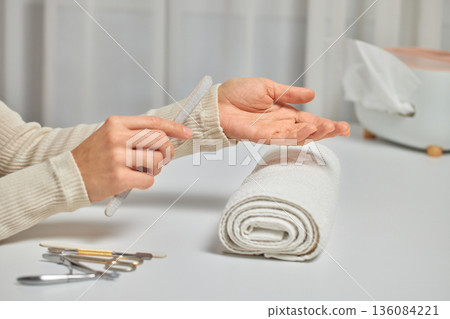 beautician with nail file prepare for nail manicure at spa center. Beautician file nails to a customer in luxury salon. 136084221