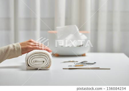 Woman enjoying a self-care beauty routine with a hand on a rolled white towel 136084234