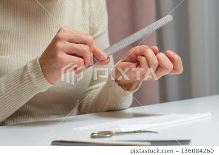 Woman performing manicure, filing her fingernails for personal care and beauty treatment Woman performing manicure, filing her fingernails for personal care and beauty treatment 136084260