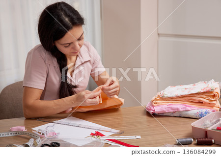 Woman carefully hand sewing fabric with a needle on a wooden table Woman carefully hand sewing fabric with a needle on a wooden table 136084299