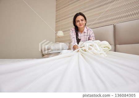Woman making bed in pajamas, starting her morning routine Woman making bed in pajamas, starting her morning routine 136084305