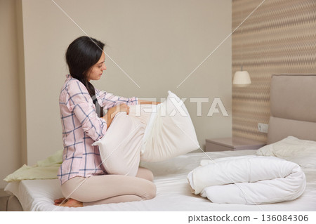 Young woman making bed, changing pillow cover during morning routine Young woman making bed, changing pillow cover during morning routine 136084306