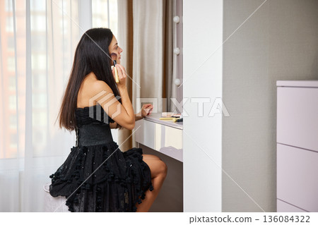 Woman applying face powder with a brush, getting ready for an event Woman applying face powder with a brush, getting ready for an event 136084322