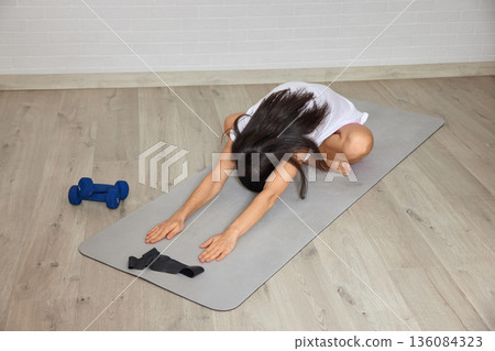 Woman performing a child's pose on a yoga mat during a home workout for wellness Woman performing a child's pose on a yoga mat during a home workout for wellness 136084323