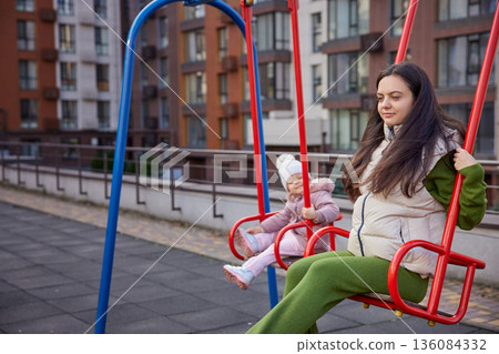 Mother and daughter swinging, having fun and bonding at the playground Mother and daughter swinging, having fun and bonding at the playground 136084332