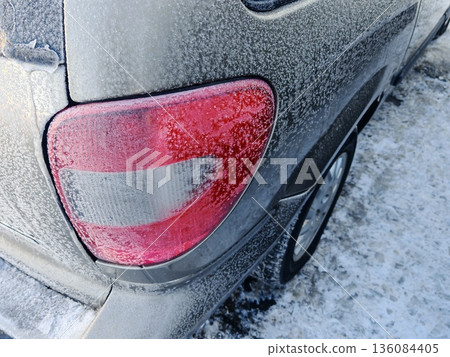 Frost-Covered Car Taillight in Winter Cold. Close-up of red car taillight glowing through thick frost and ice on snowy winter day. Frost-Covered Car Taillight in Winter Cold. Close-up of red car taillight glowing through thick frost and ice on snowy winter day. 136084405