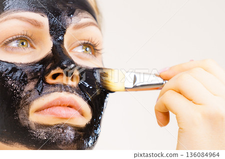 Woman applying black mud mask to face Woman applying black mud mask to face 136084964