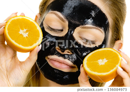 Girl black carbo mask on face holds orange fruit 136084973